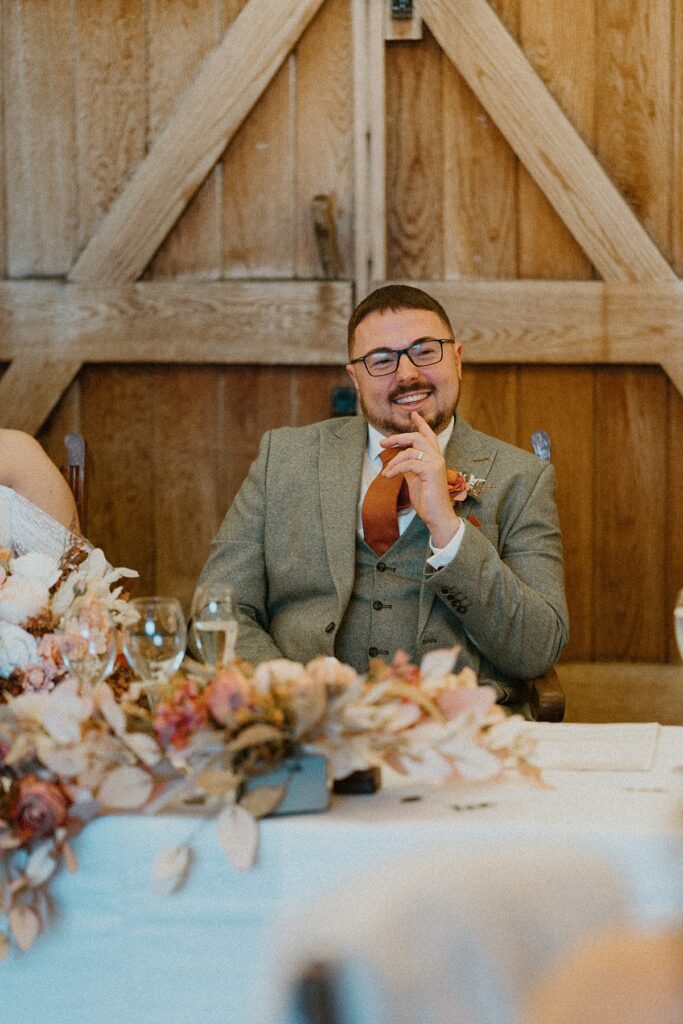 a groom laughing as his bestmen are giving their speech at his wedding