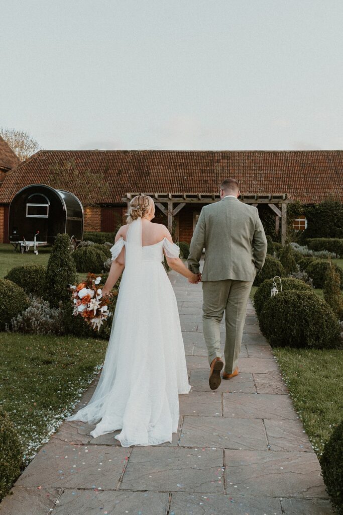 newly wed holding hands and walking away from a luxury photographer at Ufton Court Barn