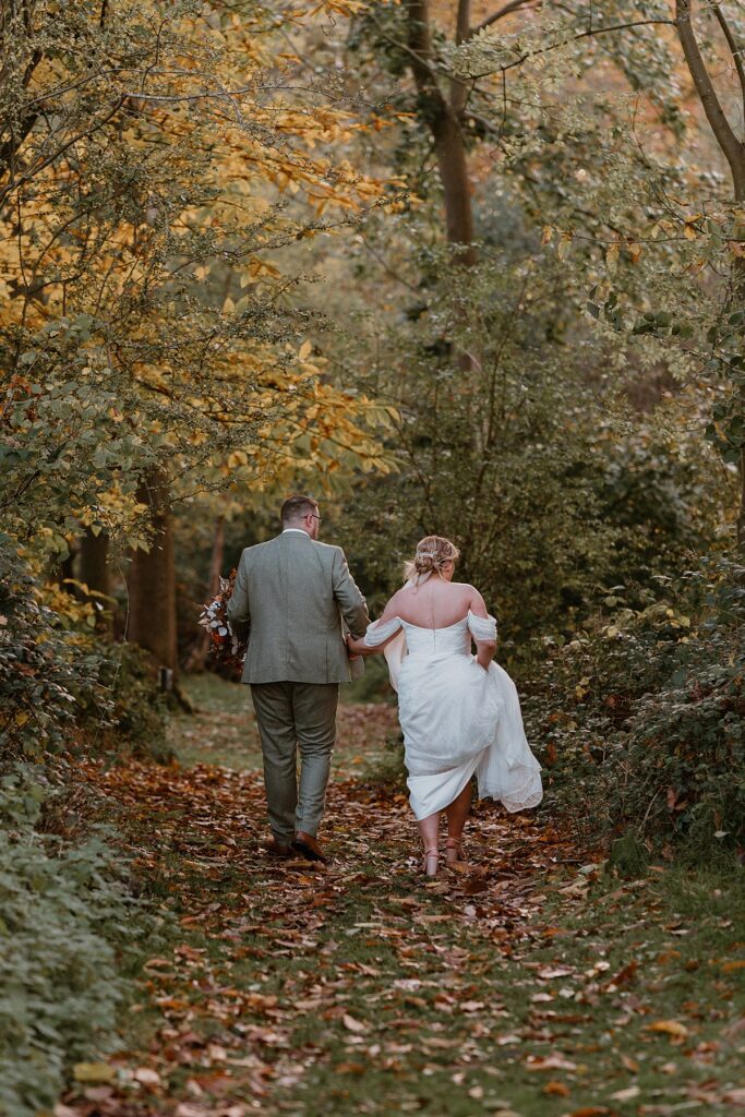 a bride and groom holding hands as they walk into woodland for couples portraits