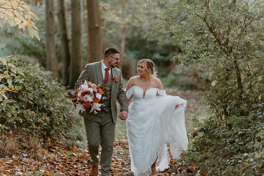 a couple of newly weds walking ad laughing she she holds up her dress in a autumn wood at Ufton Court