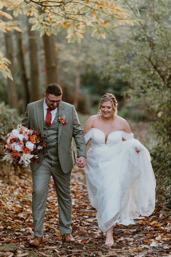 a couple of newly weds walking ad laughing she she holds up her dress in a autumn wood at Ufton Court