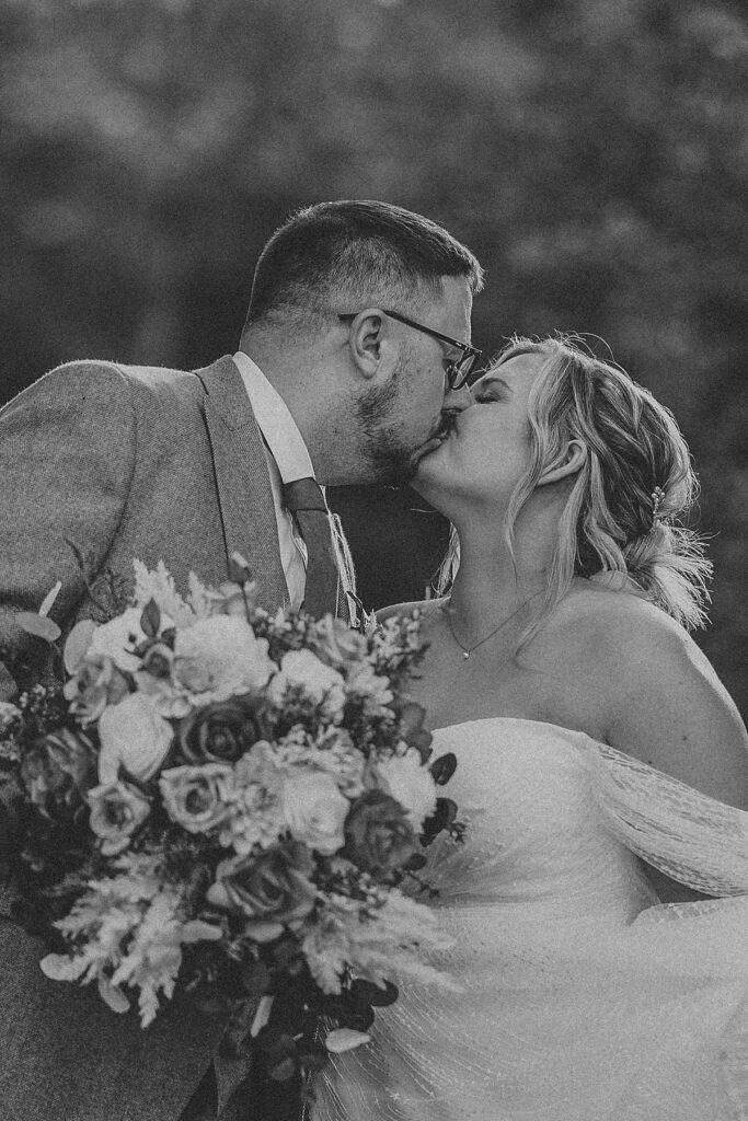 a black and white of a newly wed couple kissing each other as she holds her bouquet