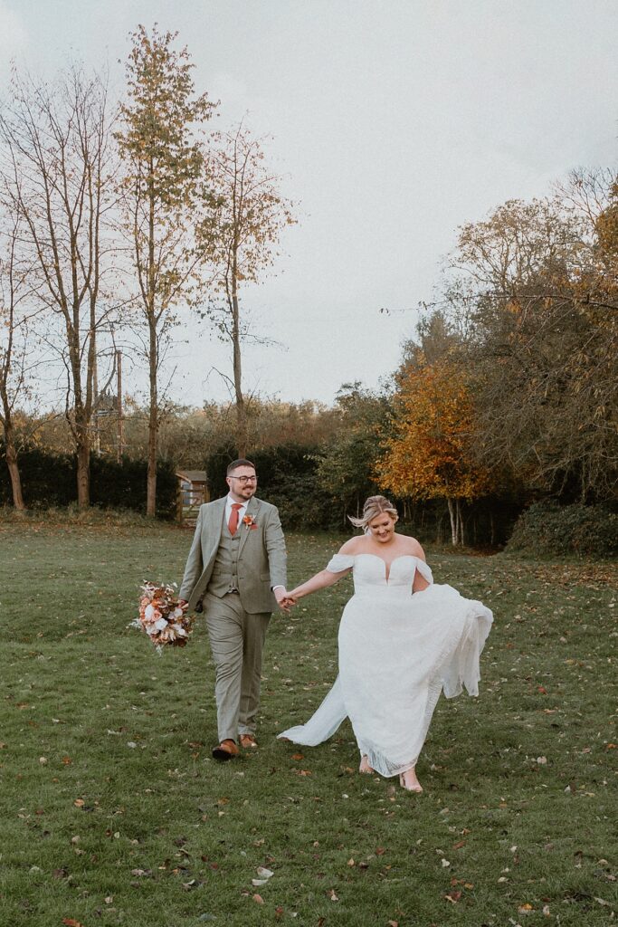 a bride leading her husband across a field at Ufton Court Barn in Aldermaston