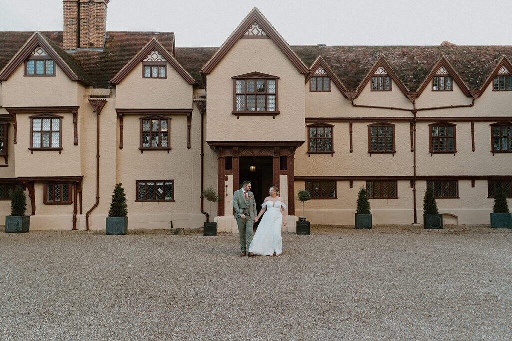 a bride and groom walking hand in hand in front of Upton Courts manor house