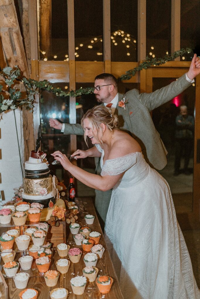 A bride and groom cutting their cake and cheering during their wedding reception at Ufton Court Berkshire