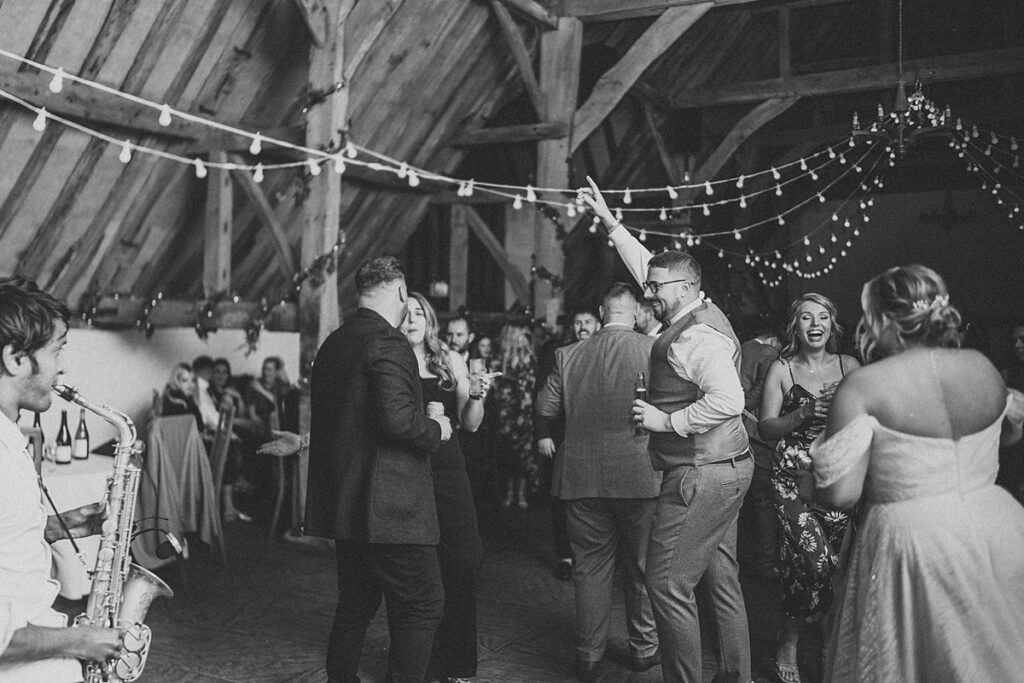 a black and white photo of a groom dancing with his guests at his own wedding party