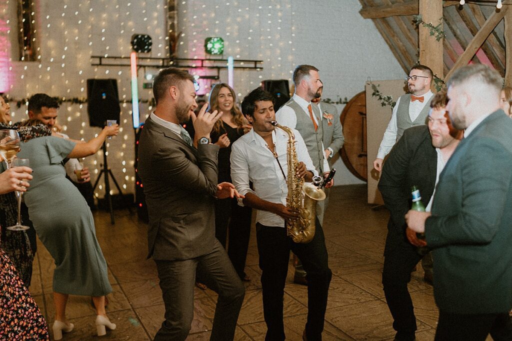 a saxophone player in the middle of a wedding party laying along with the music at Ufton Court