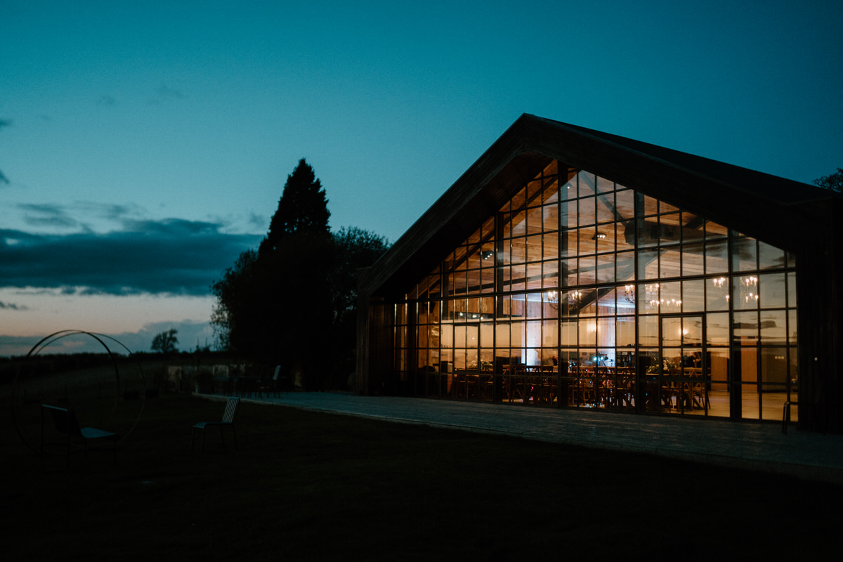 a luxury wedding barn at night showing the wedding reception happening through the window