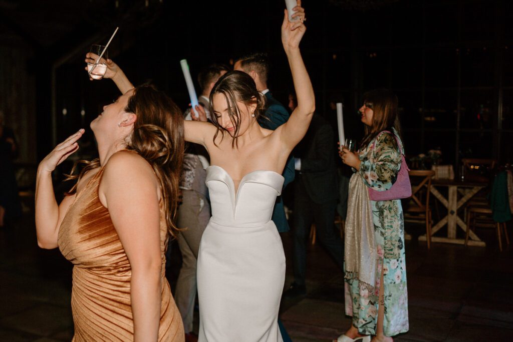 a bride throwing her hands up in the air as she dances with fellow wedding guests at her reception taken by a luxury wedding photographer 