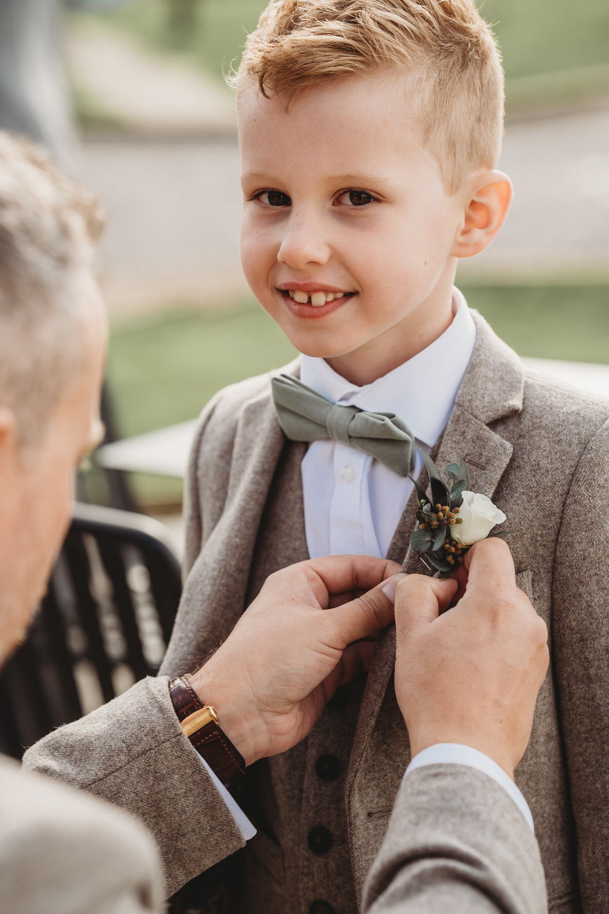 a page boy having his button hole pinned on by his dad as he smiles