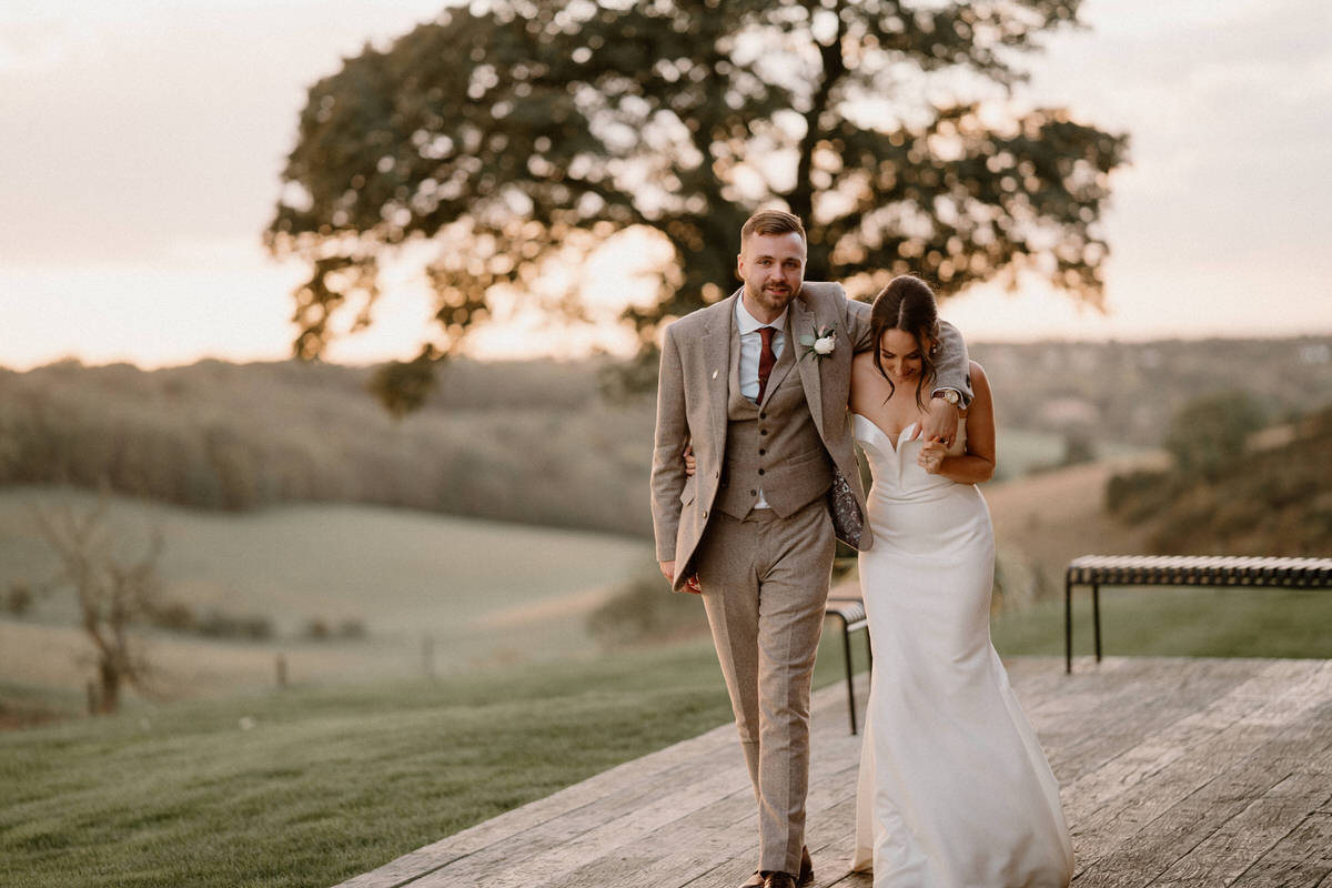 a newly wed wife and groom walking and hugging outside their surrey barn venue