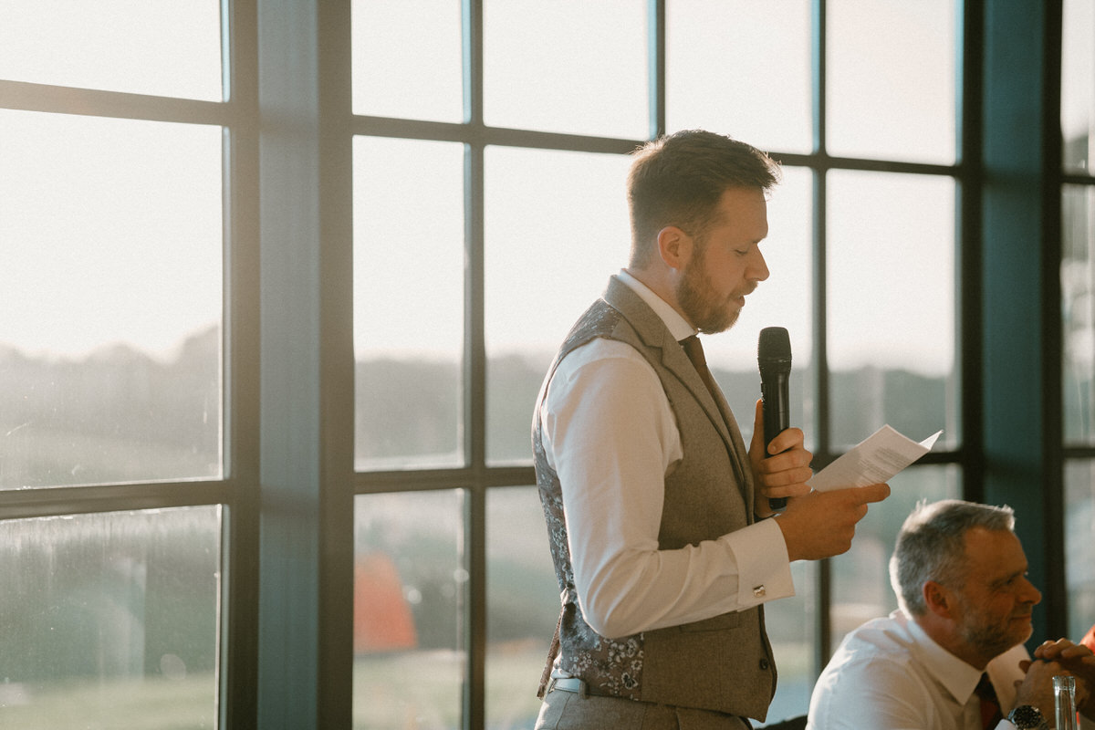 a bestman gives his speech in front of a huge set of barn windows