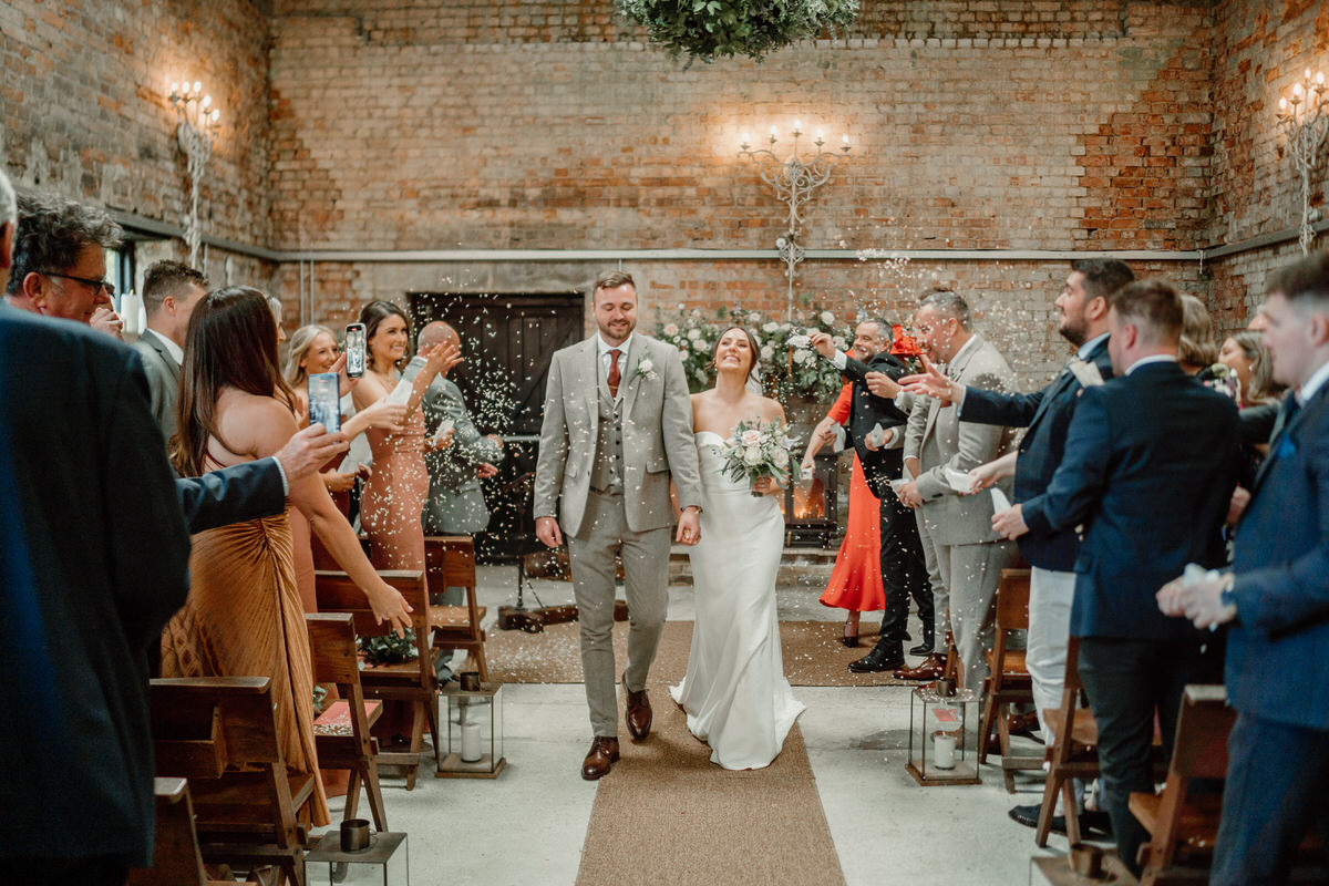 a bride and groom walk back down the aisle as the wedding party throws confetti after their wedding at a luxury surrey wedding venue as by a luxury wedding photographer