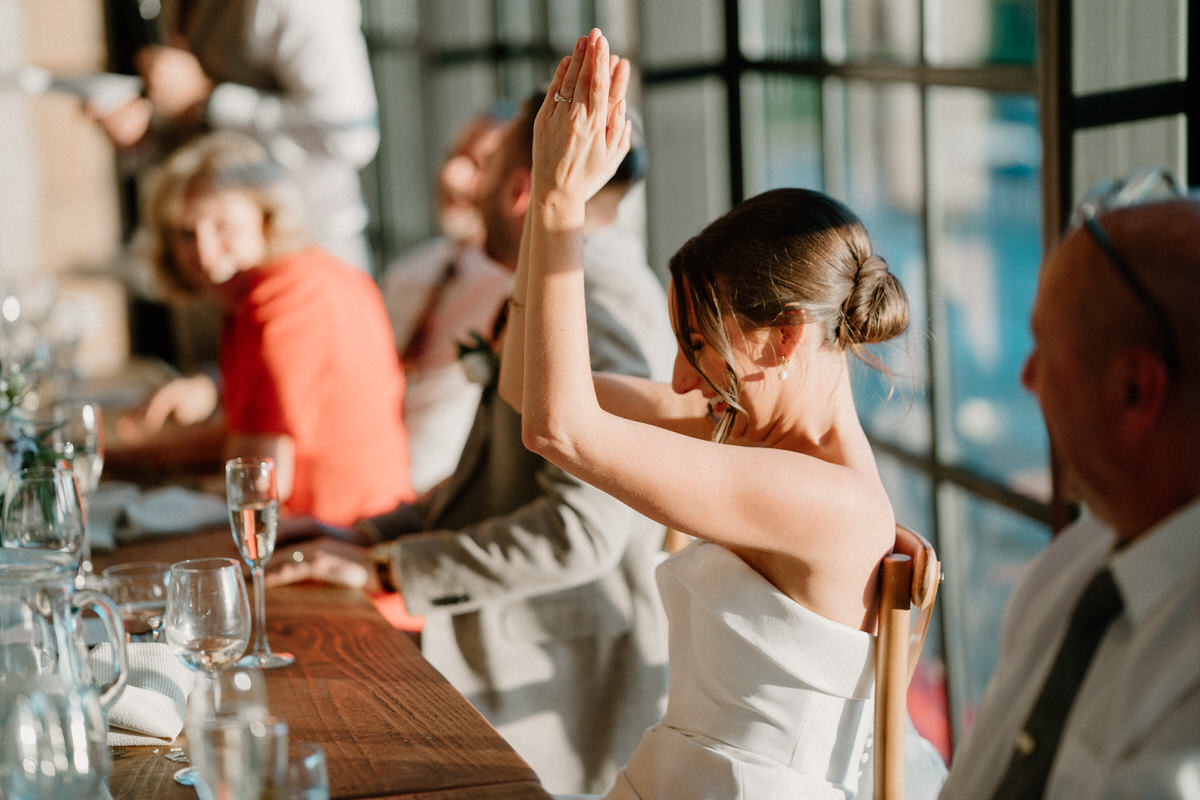 a bride raises her hand clapping as she laughs at a bestmans joke