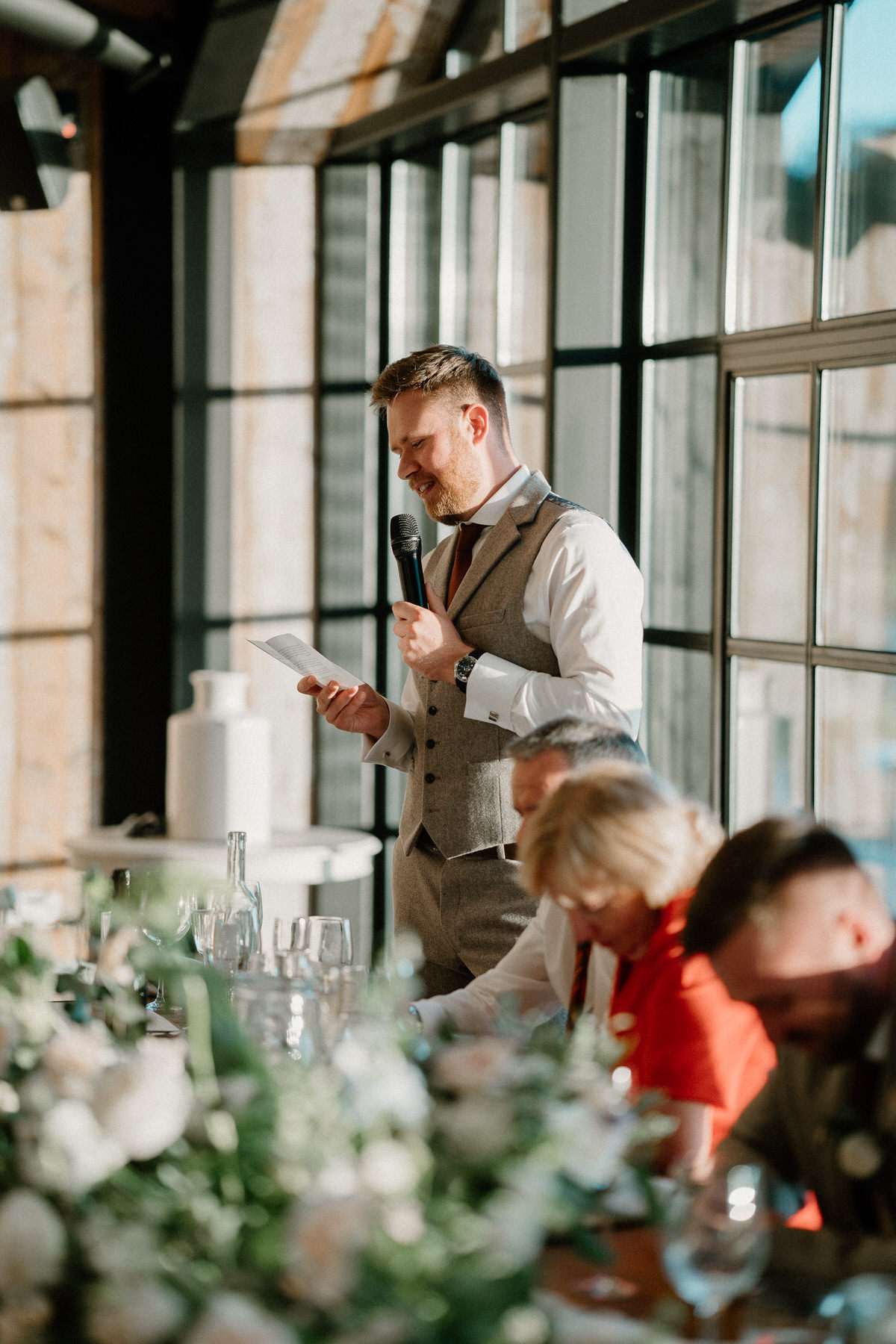 a bestman, holds a microphone as hes giving a speech to the wedding guests