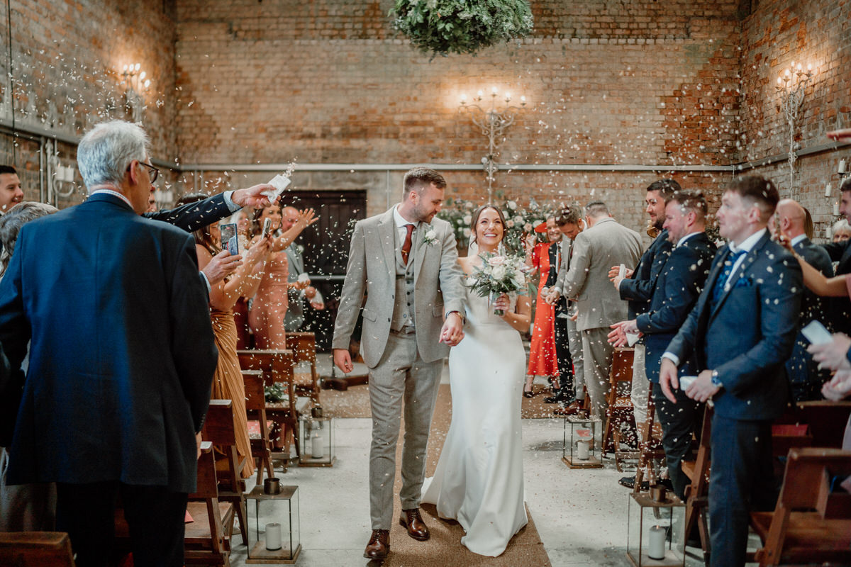 a bride and groom walk back down the aisle as the wedding party throws confetti after their wedding at a luxury surrey wedding venue