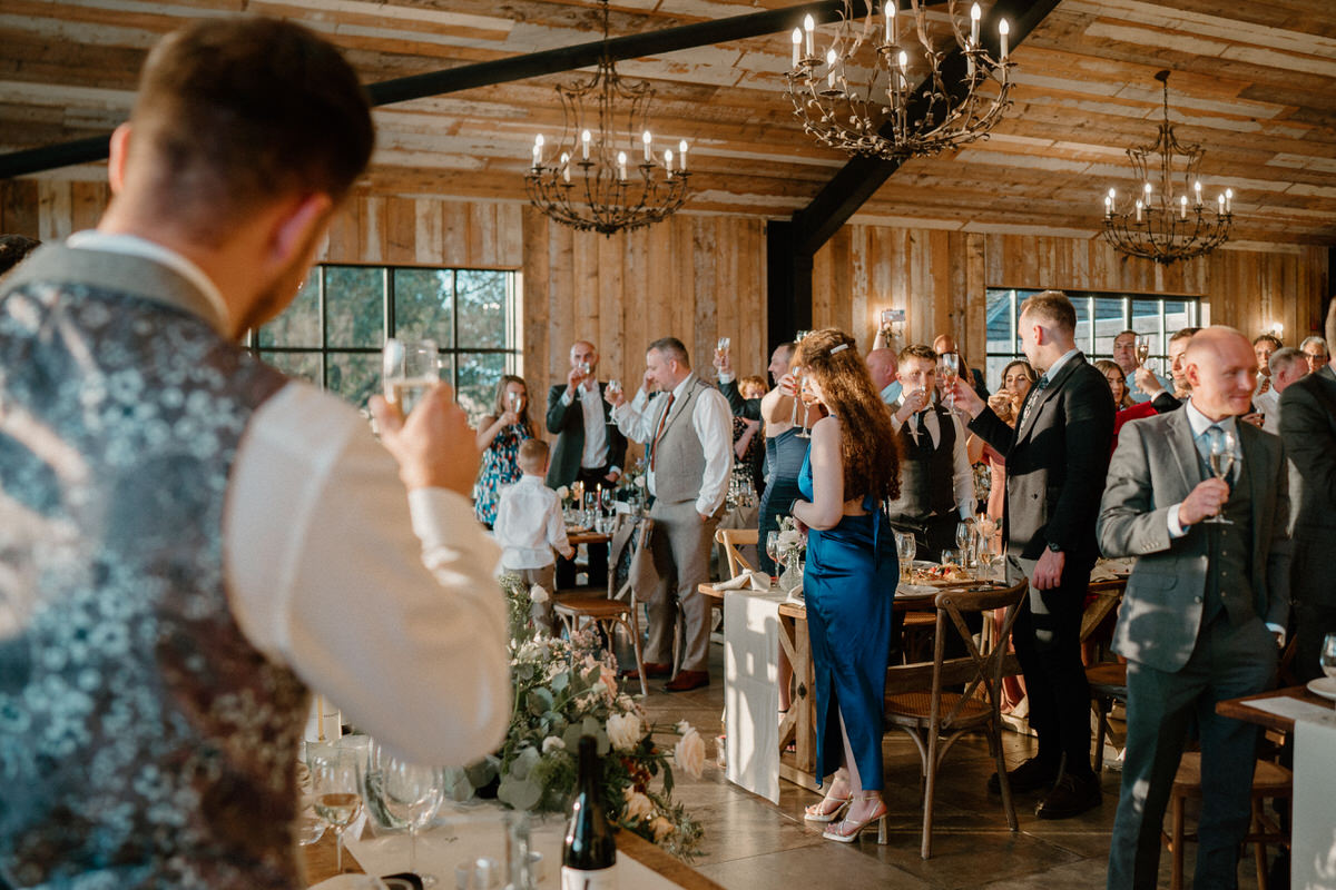 the wedding guests are on their feet clapping and raise a class during a wedding speech