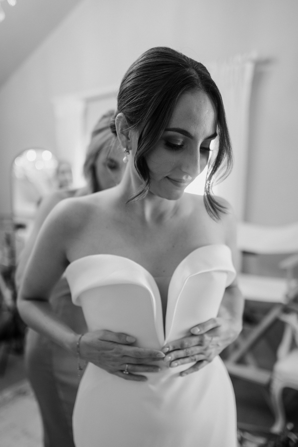 a bride holding her dress up whilst a bridesmaid does the back up ready for a luxury wedding at botley hill barn