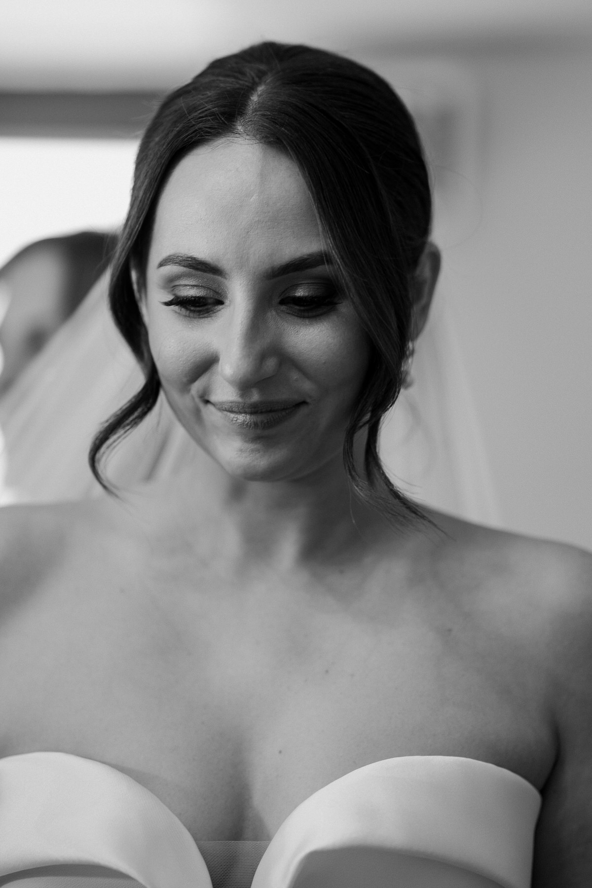 a bride looking down, thoughtfully as her bridesmaid helps her adjust her veil 