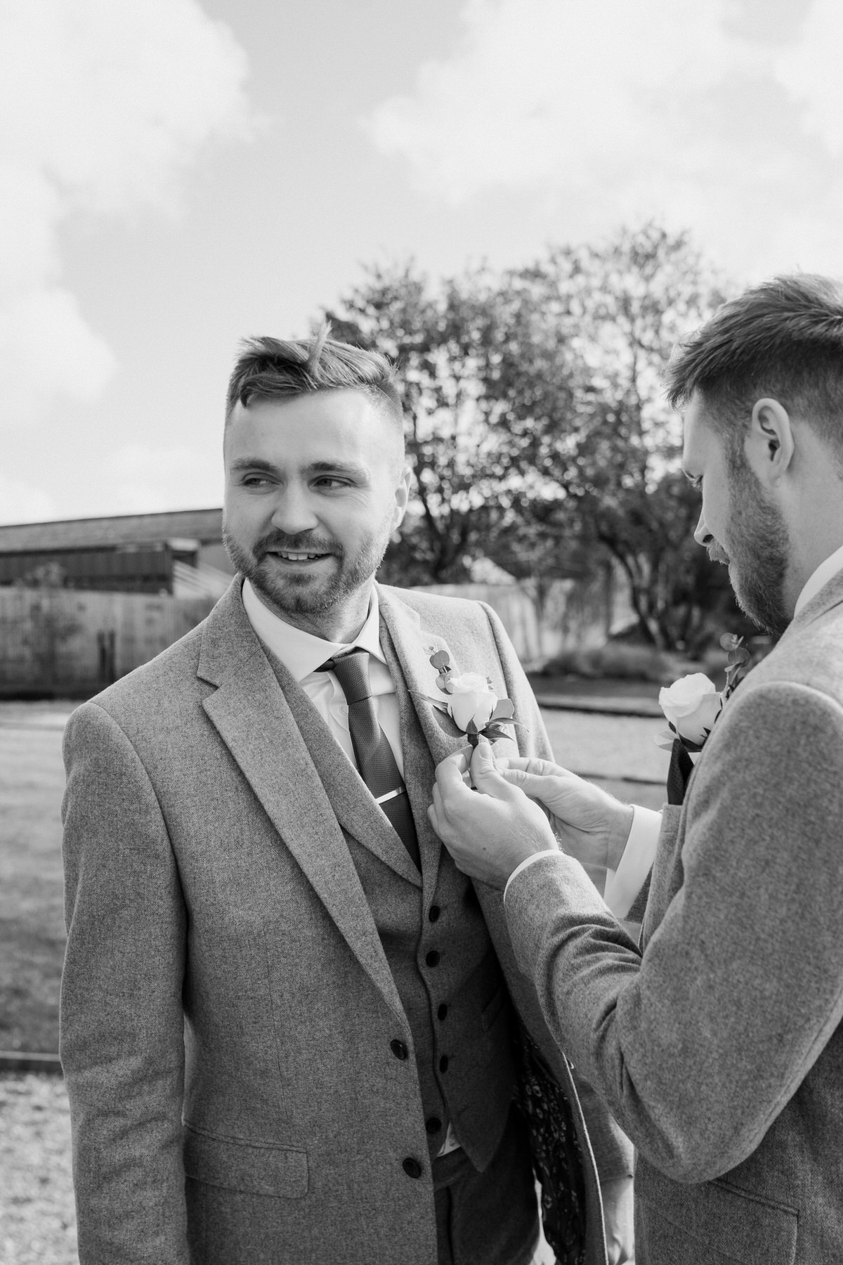 a groom having his button hole pinned on by a groomsmen for a luxury barn wedding