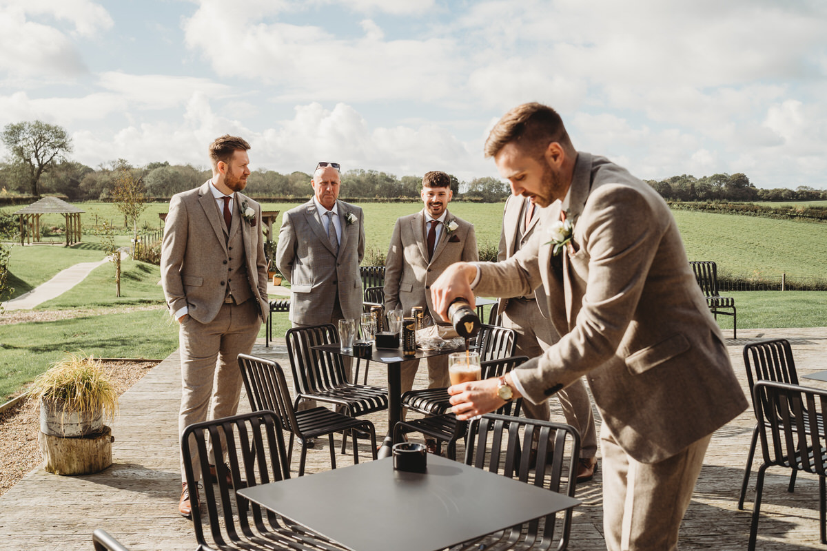 a group of groomsmen looking on as the groom pours himself a pint of guiness at Botley Hill Barn