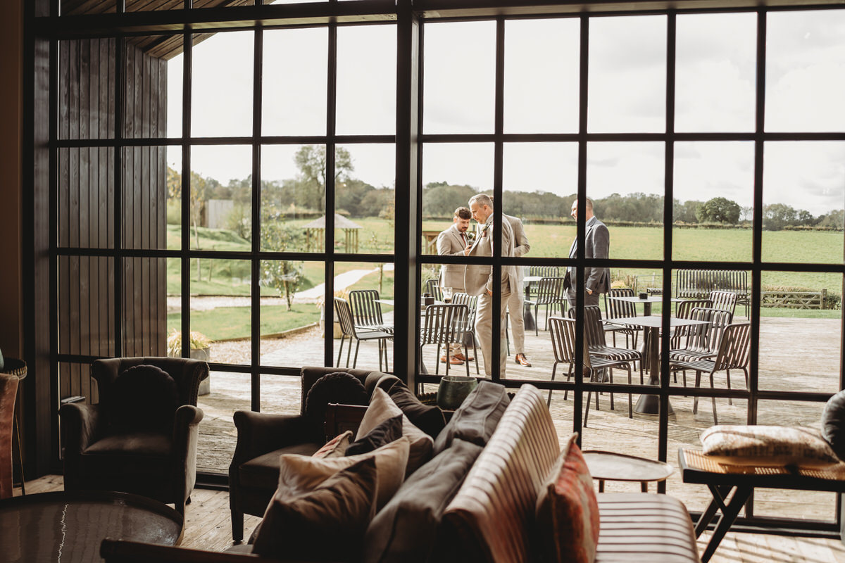 looking through a window at a group of groomsmen gathered outside on the decking at a surrey wedding venue