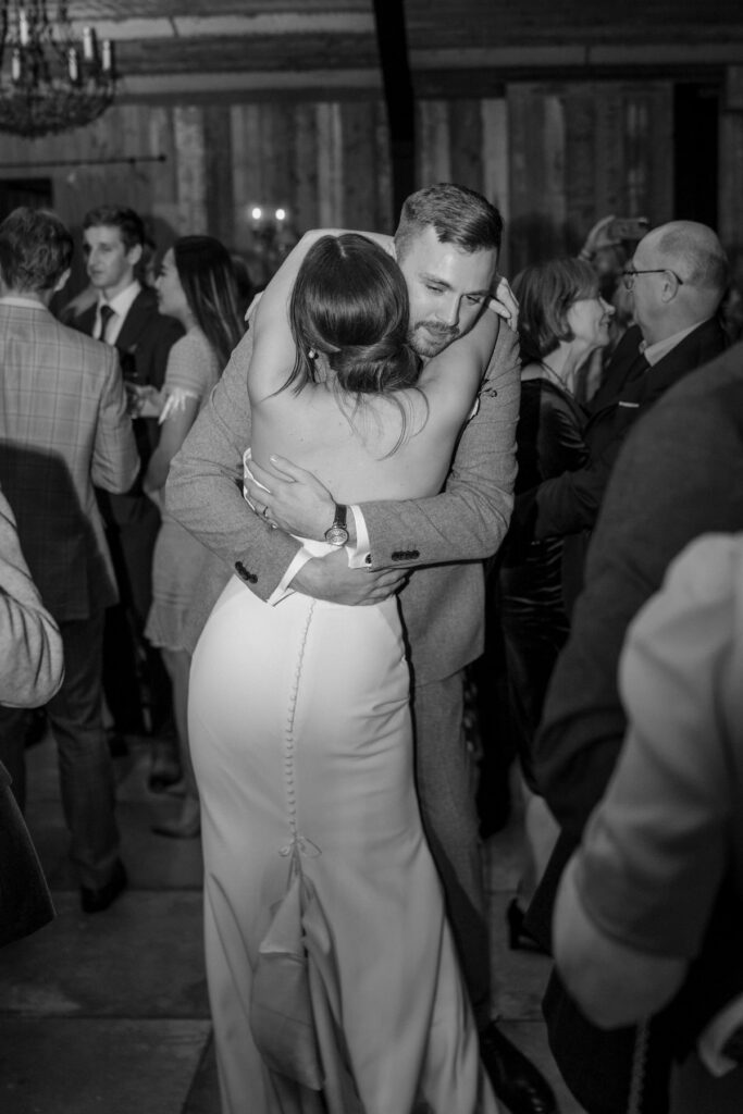 a bride and groom hug as they dance amongst a dance floor of people during their wedding reception at the luxury Botley Hill Barn