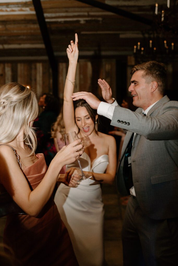 a bride throwing her hand up in the air as she dances with her wedding guests at a bride and groom dancing together in the middle of a packed dance floor of guests taken by a luxury wedding photographer