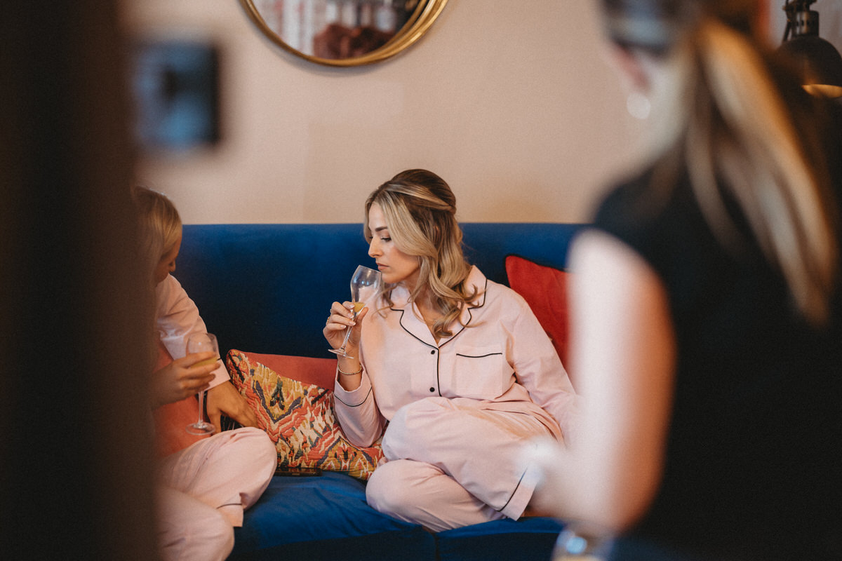 bridesmaids sat on a sofa, drinking champagne during bridal prep at a Surrey wedding venue