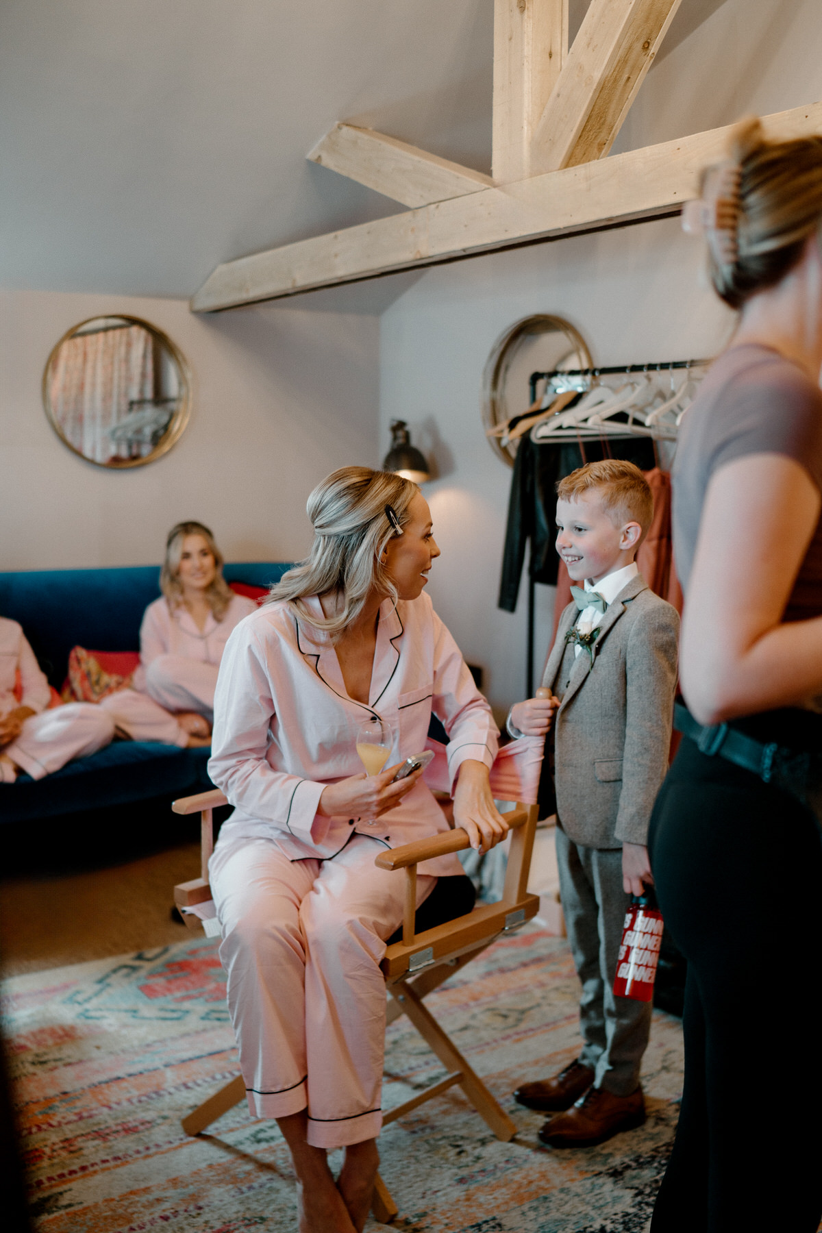 a page boy saying hi to a bridesmaid as shes sat down waiting for her make up